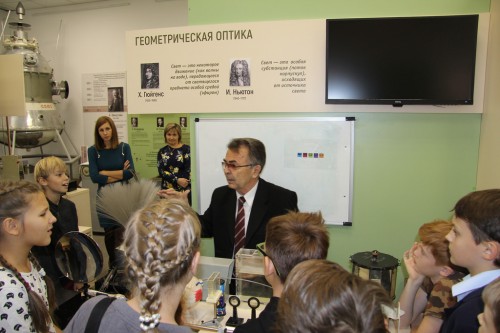 Дети и родители слушают лекцию у стенда геометрической оптики